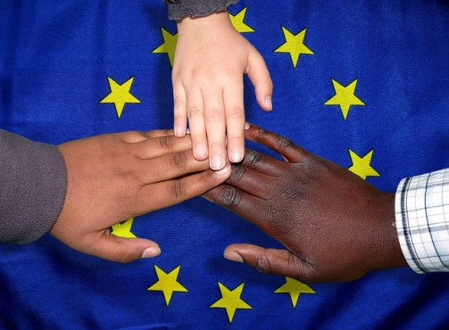 Tres manos de personas de diferentes etnias unidas rodean la bandera de la Unión Europea